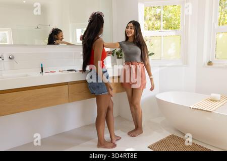 Smiling Diverse female friends greeting each other in modern bathroom, with wooden vanity Stock Photo