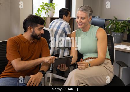 Discussing ideas Diverse coworkers sitting in modern office, using tablet and computer monitors Stock Photo