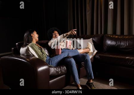 Laughing African American couple leaning on sofa in living room, holding striped popcorn tubs Stock Photo