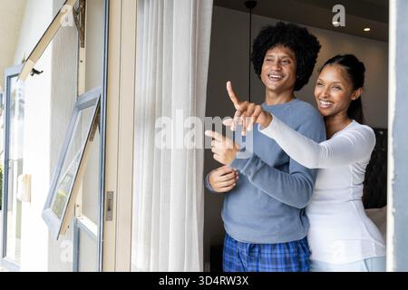 Pointing diverse couple standing near open sliding glass door in bedroom, copy space Stock Photo