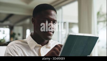 Freelancer, tablet and reading with black man on sofa for editor feedback, blog writer or research. Online review, report and remote worker or person Stock Photo
