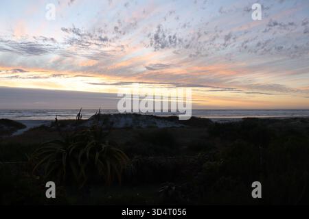 A golden sunset covering the skies of Melkbosstrand beach, South Africa, with dramatic clouds painting the evening sky in layers of color and texture. Stock Photo