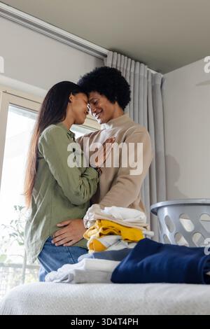 Smiling Diverse couple pressing foreheads together next to sliding glass door, with laundry basket Stock Photo