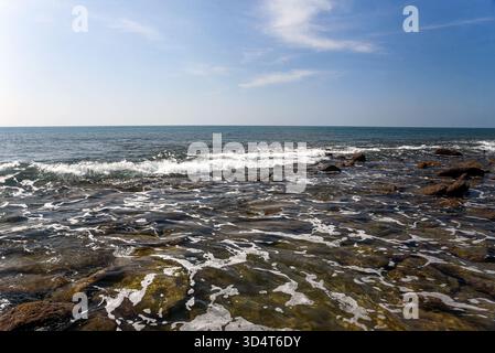 Rocky Shoreline Under Blue Sky With Gentle Waves Breaking on Stones Stock Photo