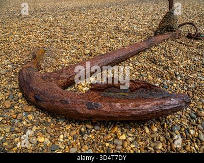 Rusty iron anchor lying on a pebble beach in morning light Stock Photo