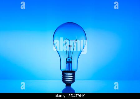 A light bulb is lit up in a blue background. The light bulb is the main focus of the image, and it is glowing brightly. The blue background creates a Stock Photo