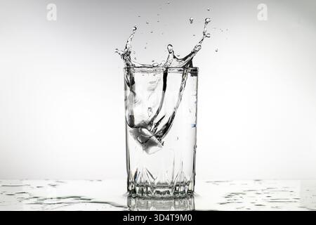 A glass of water with ice cubes in it is splashing water out of the glass. The water is cold and refreshing, and the ice cubes are melting, creating a Stock Photo