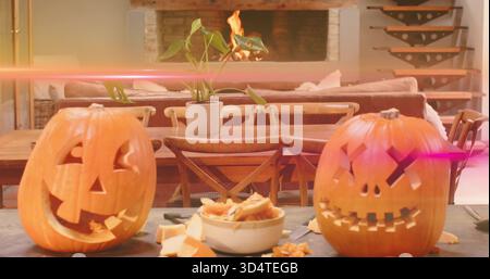 Glowing two carved pumpkins resting on tabletop at home, with bowl of guts and seeds, tools Stock Photo