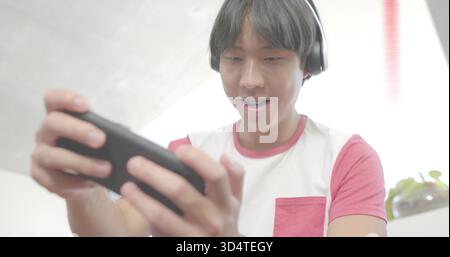 Holding smartphone in landscape, man wearing headset and red-sleeve pocket tee at home with plant Stock Photo