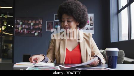 Reviewing printed pages, woman in tan blazer and red blouse sorting binder at meeting table Stock Photo