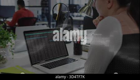 Leaning woman in white top studying laptop showing terminal data at open-plan office, headphones Stock Photo