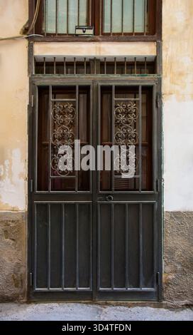 Metal door in a weathered facade in Palermo, Sicily, Italy. An outer metal door with wooden door behind it. Solid lower section, security grill upper Stock Photo