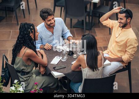 Happy multi-ethnic friends toasting with champagne at an outdoor restaurant, celebrating with a Black woman and Caucasian man smiling. Stock Photo