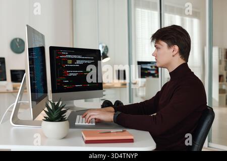 Programmer working on computer with dual monitors at white table in office Stock Photo