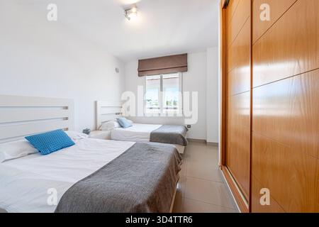 Two single beds in a bright bedroom with a window and wooden wardrobe in holiday home Stock Photo