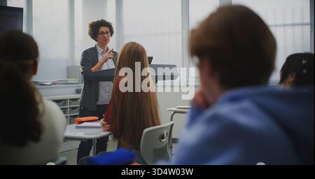 Confident Female Instructor Teaches Coding to Attentive Students, Pointing Lines Code on Interactive Display. Concept Digital Education, IT Learning Environment, and Classroom Technology. Dolly Shot. Stock Photo