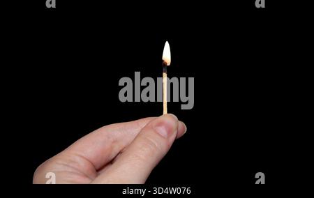 A burning match in hand. Fingers holding a burning match in the darkness. A match isolated in the black background. Stock Photo