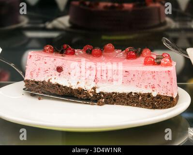 Delicious cherry cake topped with souffle and cherries set in jelly, neatly sliced into pieces and served on a white plate Stock Photo