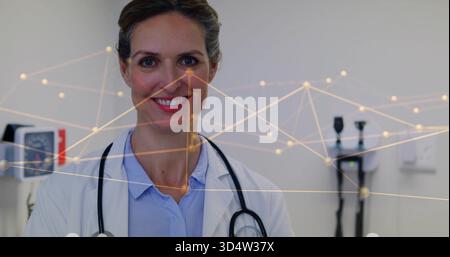 Standing mature female physician wearing white lab coat and stethoscope in clinic, network overlay Stock Photo