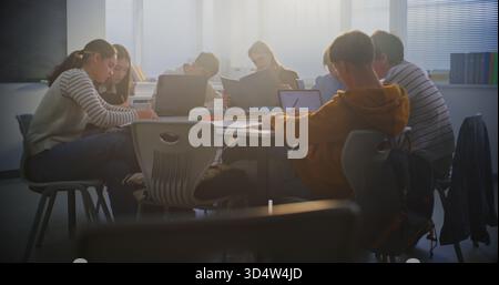 Students Collaborate on Laptops in Bright Classroom. Boy Sits Down at Table and Joins Teamwork. Concept Group Project Work, and Essential Role of Digital Learning in Modern Educational Setting. Stock Photo