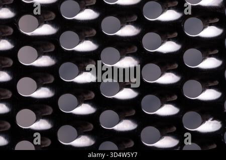 Close-up of metallic surface with repeating circular holes, creating a modern, geometric abstract pattern with high contrast lighting. Stock Photo