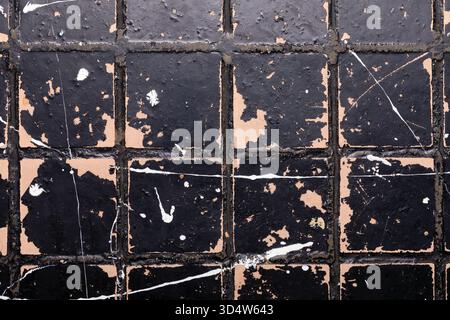 Close-up of an old black tiled surface with peeling paint and white splatters, offering a textured and weathered background for creative projects. Stock Photo