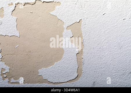 Close-up of peeling white paint on a textured wall, revealing beige underlayer. Ideal for backgrounds, renovation, or aging concepts. Stock Photo