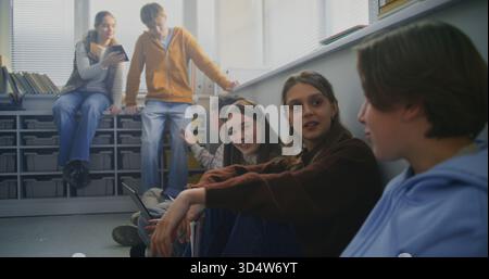 Students Sit Together on Floor Around Laptop, Sharing Ideas and Writing Notes During Collaborative Study Session. Concept Peer Learning, Open Dialogue, and Flexible Modern Classroom Environment. Stock Photo
