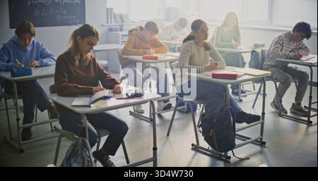 Students Writing Exam In Bright, Modern Classroom. Group of Pupils Sits at Individual Desks Focusing Intently on Taking Exam. Concentration, Independent Study, Academic Workload in Modern Education. Stock Photo