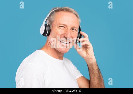 Mature Man Enjoys Music Wearing Wireless Headphones Against a Blue Background Stock Photo
