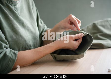 Female tailor using a seam ripper to carefully unpick the stitching on trousers. Close up of hands working in a sewing workshop. Stock Photo