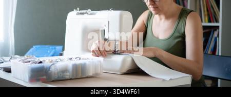 Horizontal composition. Close up of female seamstress hands skillfully operating a sewing machine, guiding fabric under the needle. Stock Photo