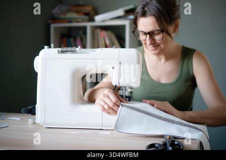 Close up of a pleased and focused female tailor working at her sewing machine, feeling satisfied with her professional sewing project. Stock Photo