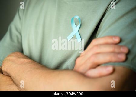 Man standing with crossed arms wearing blue satin ribbon on shirt. Concept of prostate cancer awareness in November, prevention, early diagnosis, and medical care for mens health. Stock Photo