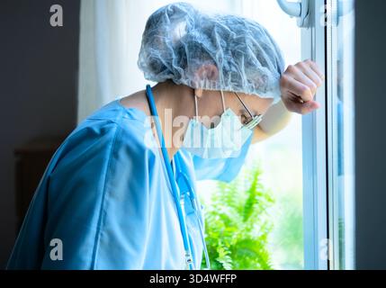 An exhausted female medical professional in uniform thinks deeply about patient care plan, showing the difficult work of hospital staff. Stock Photo