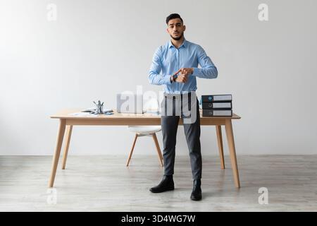 Serious Middle Eastern Manager Looks at Wrist Watch While Standing in Modern Office Stock Photo