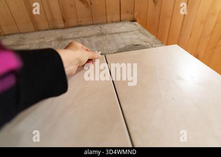 Hand placing tile spacer during ceramic floor installation in wooden house interior Stock Photo