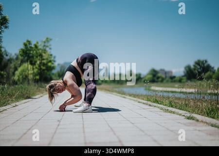Young woman practicing yoga outdoors on a sunny day along a riverside path Stock Photo