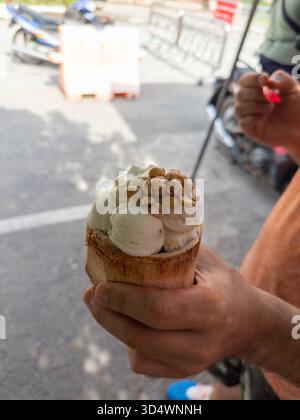 Refreshing homemade coconut ice cream, generously topped with roasted peanuts and served authentically in a natural coconut shell. A delicious tropica Stock Photo