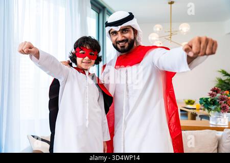 Middle-eastern family wearing traditional emirati clothing spending time together at home. Smiling middle eastern dad and kid bonding, wearing superhe Stock Photo