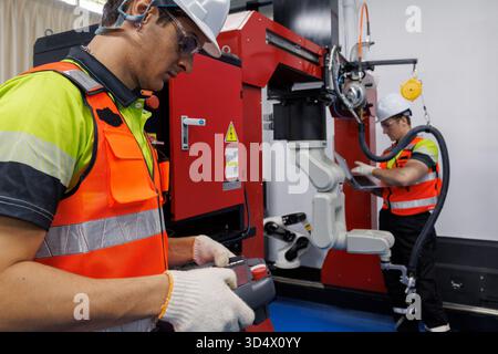 Engineer and technician working with industrial robot arm in modern factory automation system, operating robotic welding machine for smart manufacturi Stock Photo