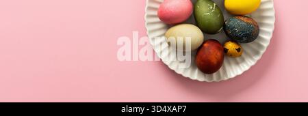 A variety of decorated Easter eggs are arranged on a circular plate against a soft pink background, showcasing vibrant colors and intricate designs fo Stock Photo