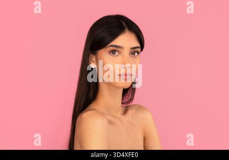 Beautiful woman with natural makeup and long hair posing against pink background Stock Photo