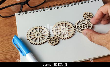 Hand Arranging Wooden Cogwheels on a Notebook: Conceptualizing Innovation, Problem Solving, and Business Strategy Stock Photo