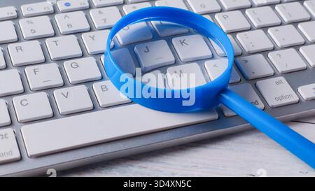 Bright Blue Magnifying Glass Resting on a Modern Wireless Keyboard for Online Search and Digital Investigation Stock Photo