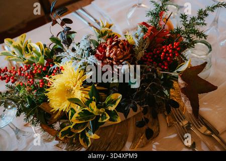 Colorful autumn floral arrangement with chrysanthemums, berries, and mixed greenery on a table setting. Ideal for festive dining, creating a warm seas Stock Photo