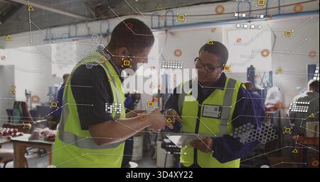 Pointing, two workers in neon-yellow vests reviewing tablet at workshop, with overlay graphics Stock Photo
