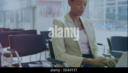 Working woman typing on silver laptop in modern lobby, wearing beige blazer and pink top Stock Photo