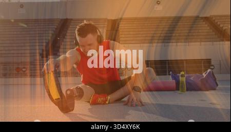 Stretching man with prosthetic blade wearing red top and black shorts on track, with headphones Stock Photo