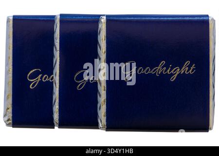 3 three wrapped individual chocolates with Goodnight inscribed on them isolated on white background - complimentary chocolate left on pillow of bed Stock Photo